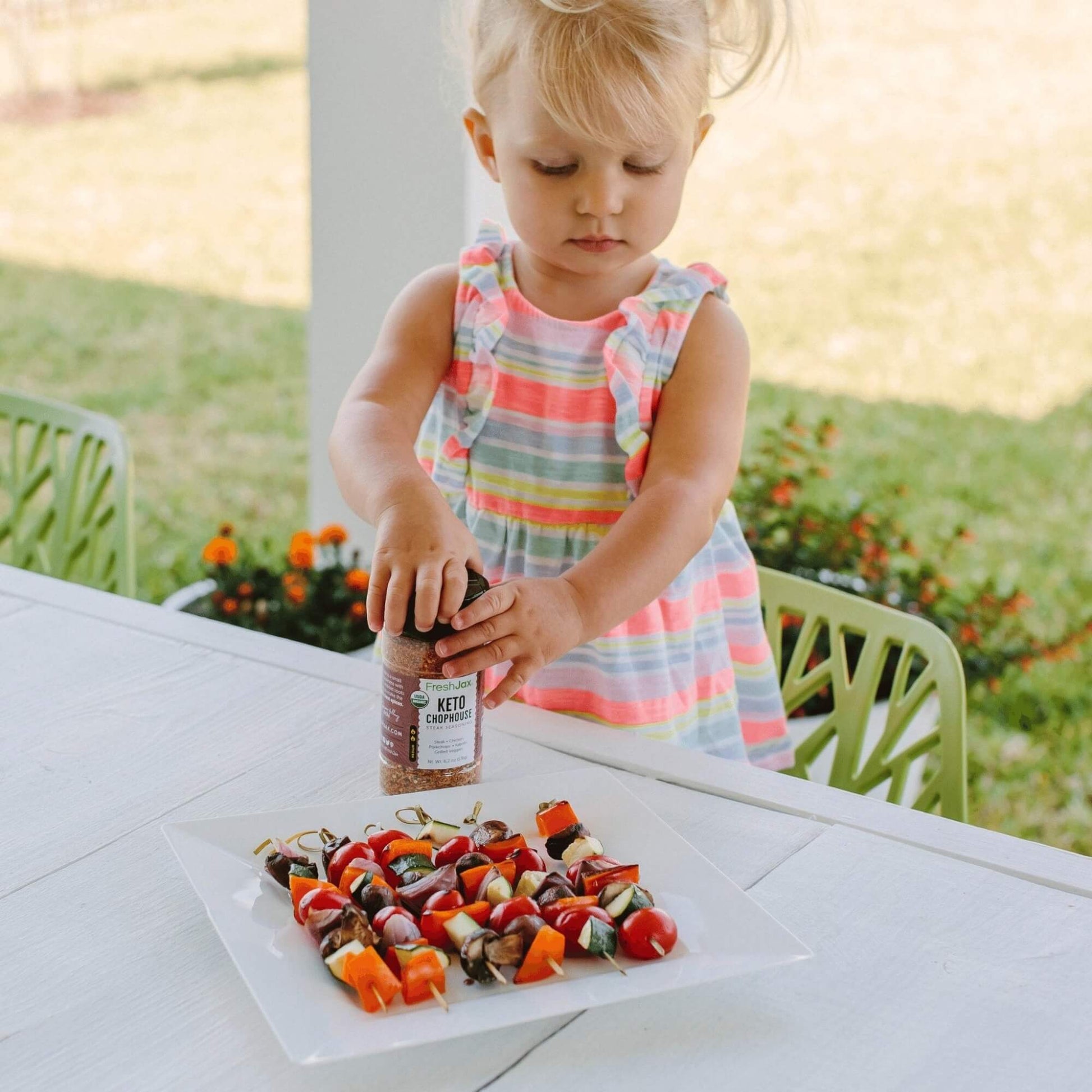 A small child putting Keto Chophouse Seasoning on veggie kabobs