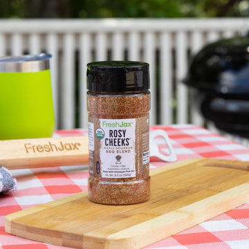 FreshJax Rosy Cheeks Maple Bourbon BBQ Rub on a cutting board next to a grill