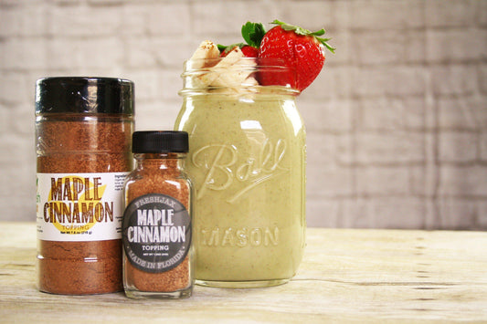 Two bottles of FreshJax Organic Maple Cinnamon Topping next to a Ball Jar filled with a maple cinnamon smoothie topped with whipped cream and strawberries.