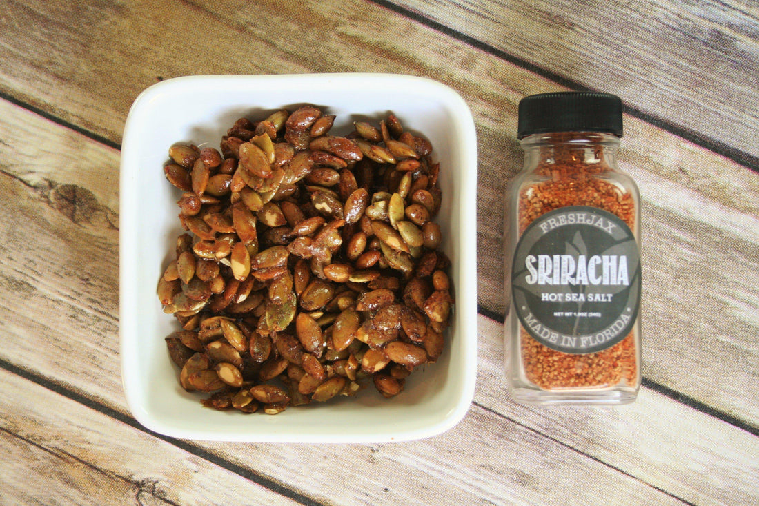 A bottle of FreshJax Sriracha Hot Sea Salt next to a bowl of sriracha pumpkin seeds. 