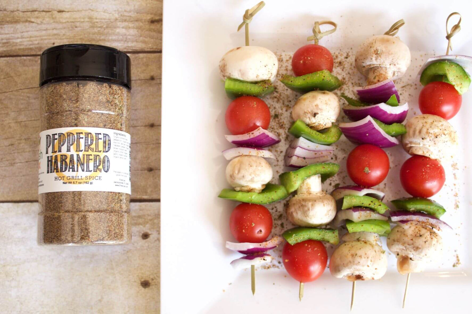 A bottle of FreshJax Organic Peppered Habanero Seasoning next to a plate of cooked veggie kabobs.