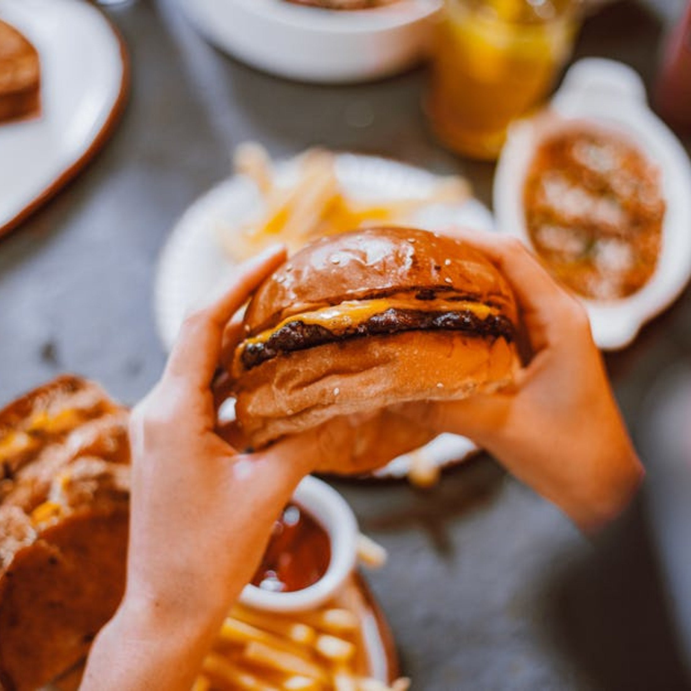 Two Hands holding a hamburger surrounded by sides