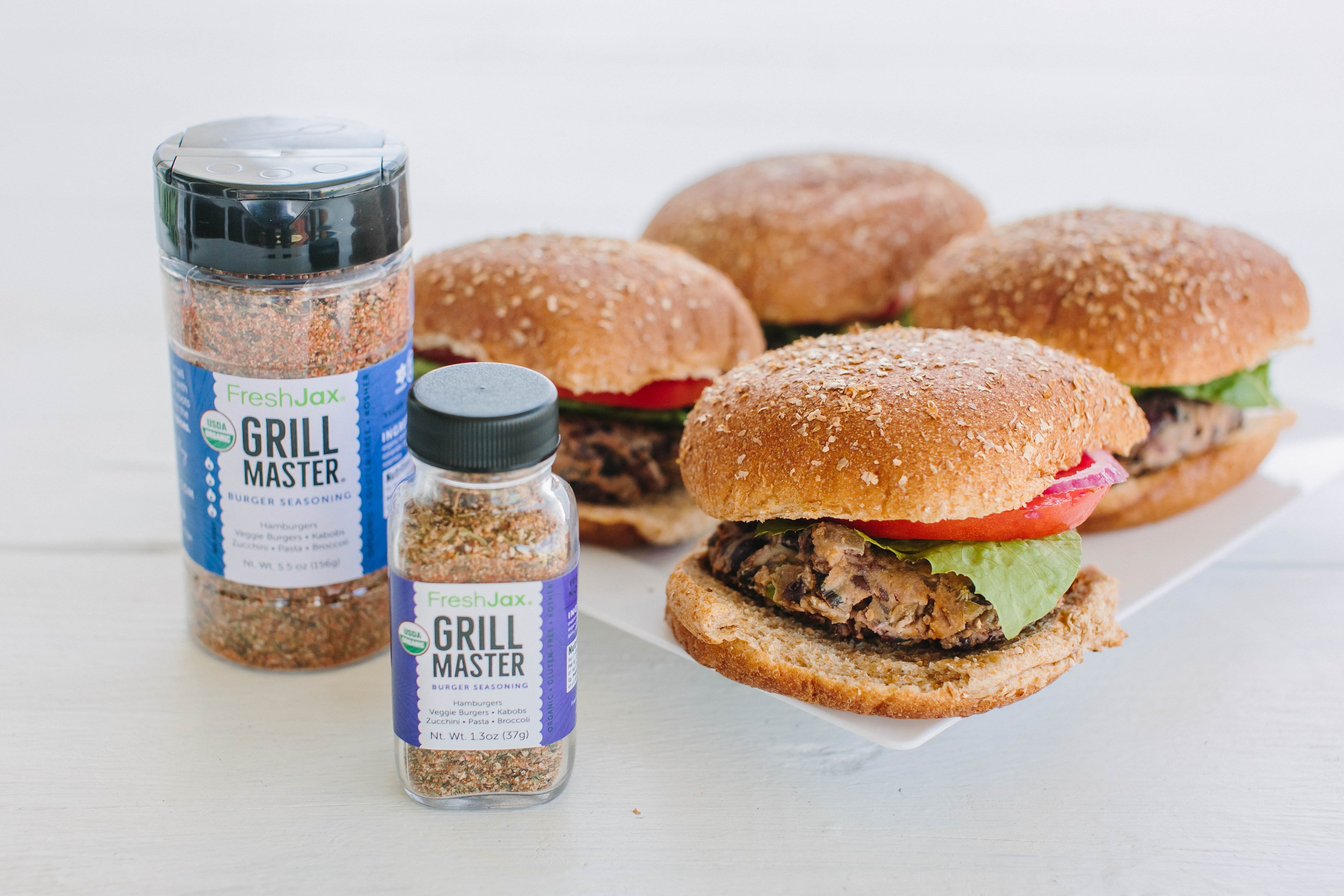 Two bottles of Freshia Grill Master seasoning with three burgers on a white surface.